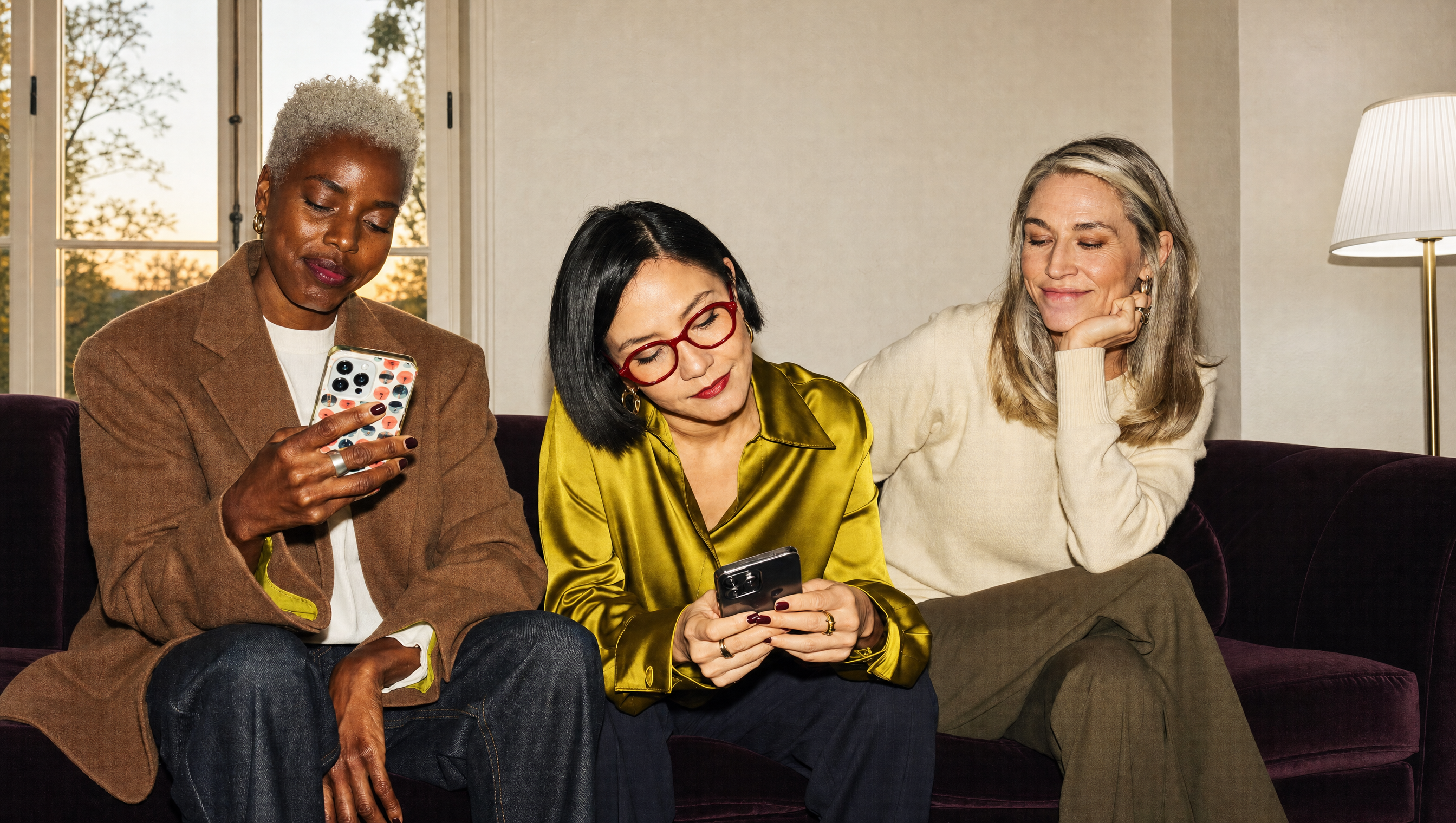 Three women on a plum sofa, two reading their phones